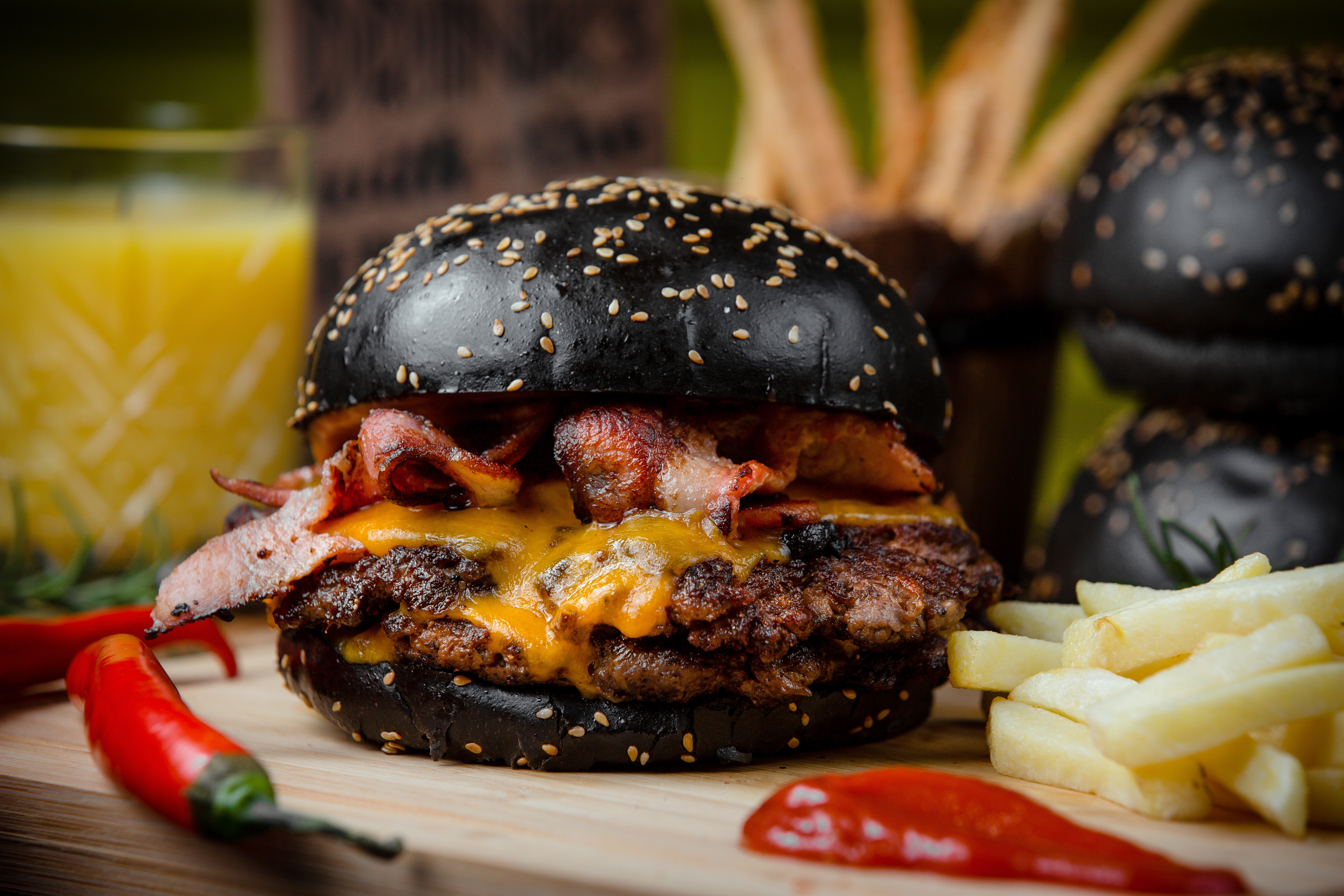 Zastaki.com - Гамбургер с черной булкой на столе с картофелем фри и красным перцем